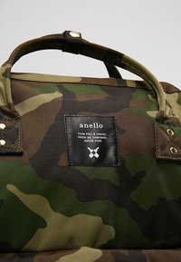 Kangaskassi, jossa on vahvat kahvat ja musta etiketti, johon on kirjoitettu valkoisella tekstillä "anello" ja "Since 2005".