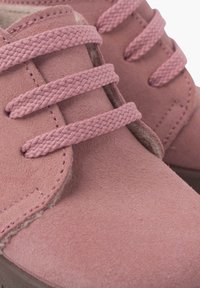 Zapatos de ante rosa que cuentan con tres cordones trenzados, un diseño redondeado y un acabado texturizado. La suela es oscura, contrastando con la parte superior.