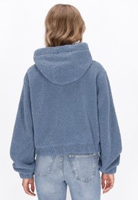 Felpa con cappuccio accorciata in morbido fleece blu chiaro con una superficie testurizzata, maniche oversized e una vestibilità rilassata. Presenta un cappuccio sul retro.