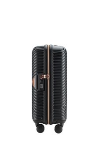 Valigia rigida nera con texture a coste, zipper rosa dorato e lucchetto. Dotata di quattro ruote per una mobilità facile.