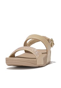 Beige sandalen met twee brede banden, waarvan één versierd is met heldere rhinestones, een platte zool en een enkelband met een metalen gespsluiting.