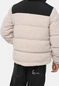 Giacca puffer in pelliccia sintetica beige chiaro con la parte superiore nera, caratterizzata da una superficie testurizzata e dettagli a coste all'orlo.