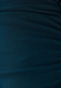 Gros plan sur un tissu texturé bleu sarcelle foncé avec de légers plis et des ombres douces.
