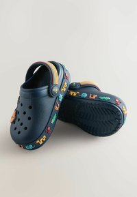 Zoccoli blu navy in gomma con fori di ventilazione, decorati con charm colorati a tema animale e accenti a strisce sulla fascia.