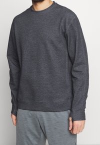 Sudadera de cuello redondo en gris oscuro con mangas largas, puños acanalados y un corte relajado, fabricada con una tela suave y ligeramente texturizada.