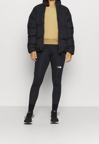 Černá puffy bunda, béžový svetr s kulatým výstřihem a černé legíny s bílým logem. Černé sportovní boty se šněrováním. Jednoduchý, štíhlý design.