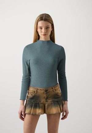Teal, ribbet langermet topp med høy hals, parret med et kort, utsvingt denimskjørt i en gradiant fra brun til falmet svart.