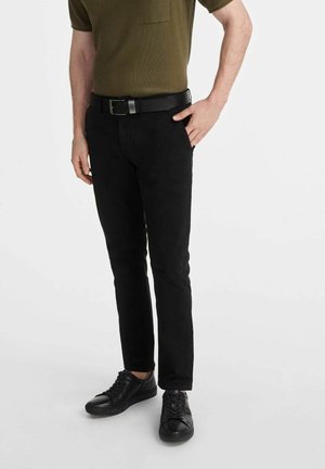 Czarne bawełniane spodnie o dopasowanym kroju, z przednią kieszenią, w komplecie z czarnym paskiem i czarnymi sneakersami. Gładka tekstura, minimalistyczny design.