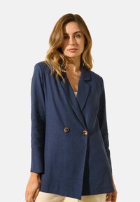 Blazer bleu marine à double boutonnage avec de grands boutons marron, revers à cran et manches longues, fabriqué à partir d'un tissu lisse au toucher doux.