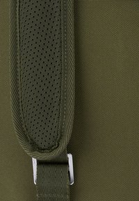 Olívazöld szövet táska, texturált, párnázott pánttal, hálós részletekkel és fémcsattal. Sima felület, finom varrással.