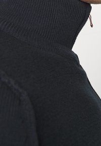 Ciemnoniebieski sweter z wysokim kołnierzem, wykonany z rypsowego materiału, o gładkiej fakturze i subtelnych detalach przeszycia.