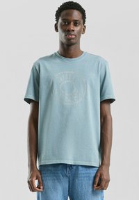 T-shirt en coton bleu clair à manches courtes et col rond. Présente un motif délavé au centre et une coupe décontractée.