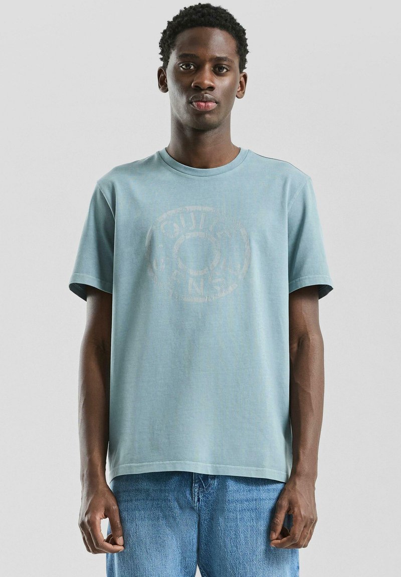 T-shirt en coton bleu clair à manches courtes et col rond. Présente un motif délavé au centre et une coupe décontractée.