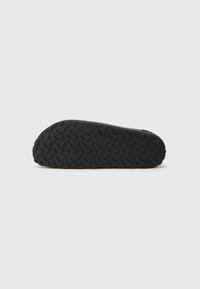 Semelle de chaussure en caoutchouc noir avec un motif ondulé, présentant des rainures profondes pour une meilleure adhérence. Bords lisses et forme légèrement arrondie.