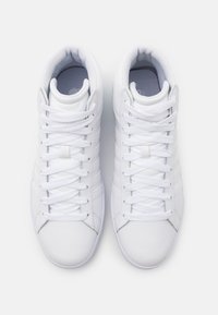 Un par de zapatillas altas, limpias y blancas, con cordones blancos, cuellos acolchados y una parte superior sintética suave, vistas desde arriba sobre un fondo blanco.