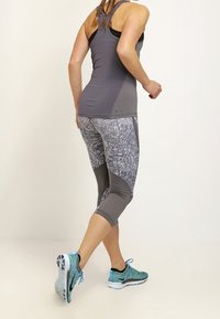 Gray athletic tank top and patterned capri leggings with geometric designs; features turquoise athletic shoes with black accents.