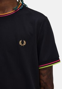 Polo negro hecho de material texturizado. Presenta un logo dorado en el pecho y acentos a rayas coloridos en el cuello y las mangas.
