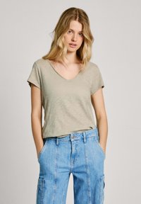 Camiseta de cuello en V, de manga corta, en un suave color verde oliva claro, hecha de una tela suave, combinada con jeans azules de cintura alta que cuentan con bolsillos laterales y detalles en las costuras.