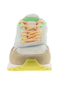 Zapatilla de deporte beige claro con suela y cordones amarillos, lengüeta verde en el talón y diseño de hoja azul bordada en los laterales, vista frontal.