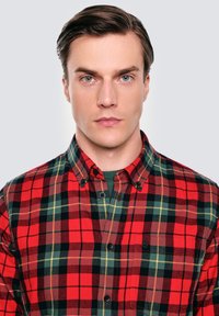 Czerwona i zielona koszula w kratę z kołnierzykiem zapinanym na guziki, z czarnymi guzikami i kieszonką. Miękka tekstura i dopasowany krój z wielokolorowymi wzorami.