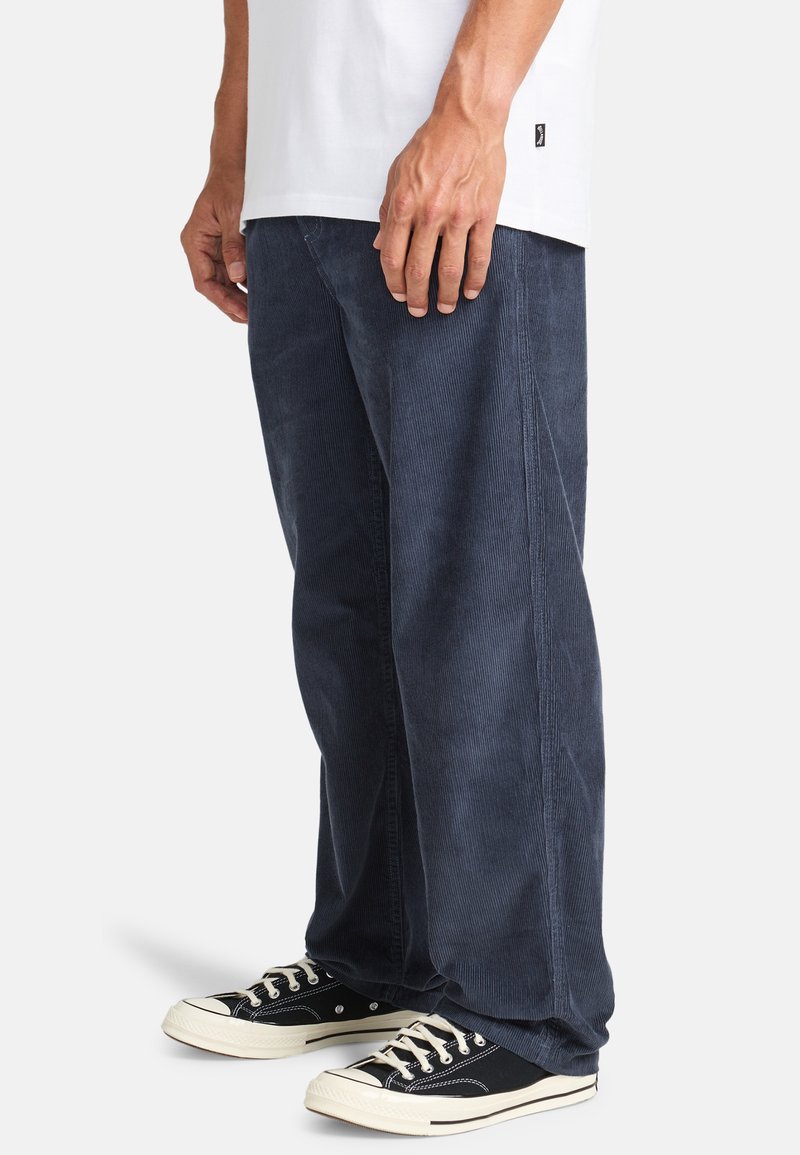 Navy corduroy pants with a loose fit, visible texture lines, and side seam detailing, paired with black canvas sneakers.