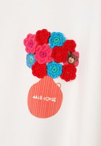 Biely textil s farebným háčkovaným kvetinovým vzorom v ružovej, červenej a modrej farbe, s pruhovaným červeným kvetináčom s motívom medveďa.