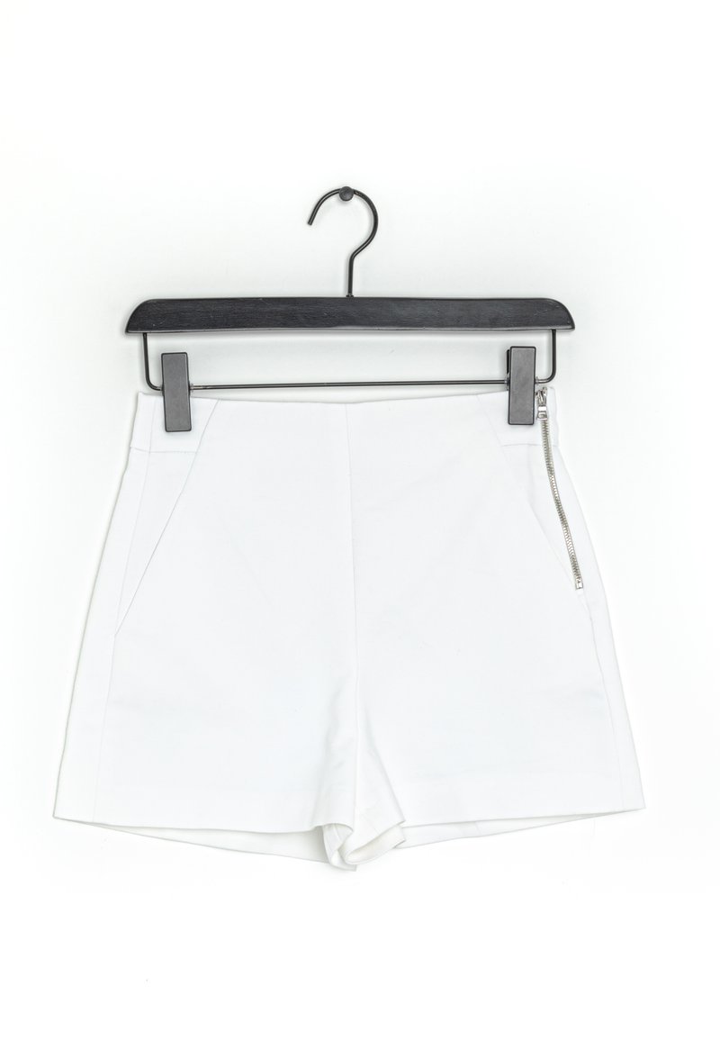 Shorts blancs sur un cintre noir, avec une poche zippée, un tissu lisse, un design ajusté et une coupe droite.