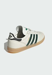 Biele kožené tenisky s tromi zelenými pruhmi, čiernym opätkom, gumovou podrážkou a polstrovaným jazykom s logom a textúrovaným dizajnom.