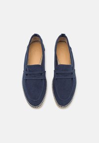 Zapatos tipo mocasín de lona azul marino con diseño de slip-on, que cuentan con una suela de yute cosida y un interior suave. Sin adornos adicionales.