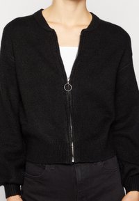 Czarny krótki sweter wykonany z fakturowanej dzianiny, z okrągłym dekoltem i przednim zamkiem błyskawicznym z srebrnym pierścieniem jako uchwytem.