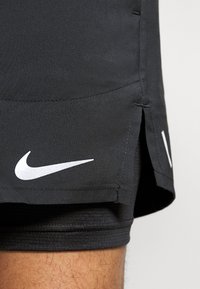 Pantalones cortos deportivos negros hechos de tela ligera, con un logo blanco de Nike en forma de swoosh, detalles de costura y aberturas laterales para facilitar el movimiento.