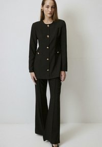 Black tailored suit featuring a fitted jacket with gold buttons and two front pockets, paired with flared pants. Smooth fabric texture.