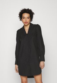 Vestido preto com um colarinho grande e ornamentado. Apresenta mangas bufantes e uma frente com botões. O tecido é liso com um ligeiro brilho.
