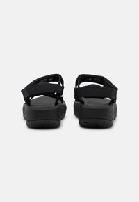 Svart sandal med texturerad gummisåle, justerbara tygremmar och dämpad innersula. Funktioner inkluderar en modern design och hållbar hårdvara.