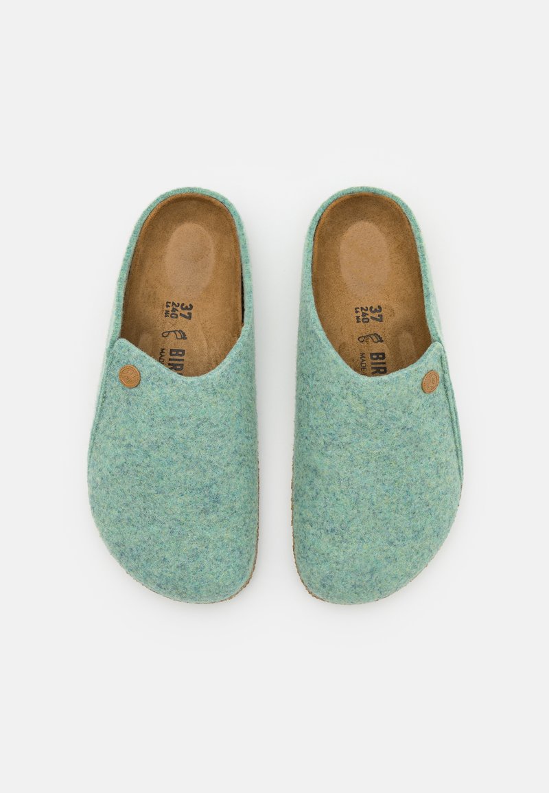 Paar von Hausschuhen in Größe 37 aus hellblauem Filz, mit braunen Innensohlen, jeweils mit einem kleinen runden Logo-Knopf auf der Außenseite.