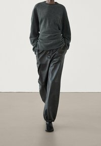 Pull en maille gris foncé à coupe ample et texture plissée, associé à un pantalon en cuir noir avec une taille élastique.