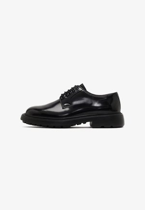 Chaussures en cuir noir avec une finition brillante, bout rond, laçage à six œillets, et semelle en caoutchouc robuste dotée de motifs de crampons profonds.