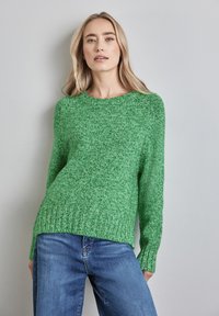 Grüner Strickpullover mit langen Ärmeln und geripptem Saum. Hat ein strukturiertes Finish und ein Rundhalsausschnitt-Design. Kombination mit blauen Jeans.