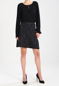 Zwarte blouse met lange mouwen en een sleutelgaatje-halslijn, gecombineerd met een zwart-witte tweedrok met een uitlopende vorm en een gestructureerd patroon.