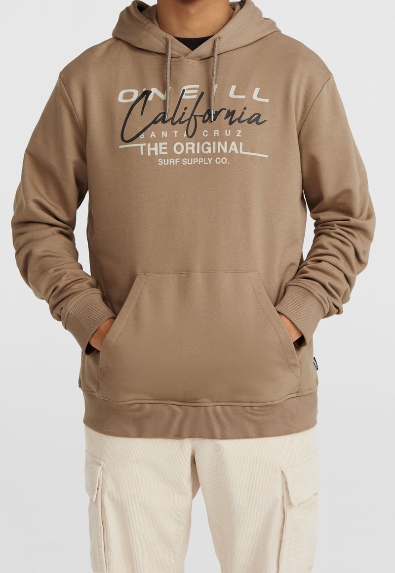 Personne portant un sweat à capuche beige avec poche avant et texte "O'Neill California Santa Cruz The Original Surf Supply Co." ainsi qu'un pantalon cargo beige clair.