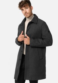 Gray wool coat with a classic collar, front button closure, side pockets, and a streamlined silhouette. Model wears a light turtleneck underneath.