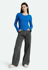 Top azzurro a maniche lunghe con scollatura a barca, abbinato a jeans in denim grigio a gamba larga e sneaker bianche.