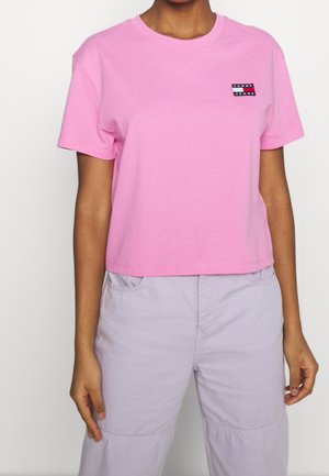 Personne portant un t-shirt court à manches courtes rose avec un petit logo Tommy Jeans et un pantalon taille haute violet clair.