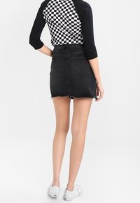 Jupe en denim noir avec un ourlet effiloché, assortie à une chemise raglan à carreaux noir et blanc. Des baskets blanches complètent la tenue.