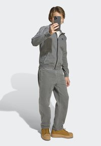 Gray zip-up jacket with side stripes and matching pants. Features elastic cuffs and waistband, paired with tan boots and a smartphone.
