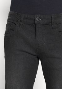 Pantalones vaqueros de mezclilla negra con una textura suave, que cuentan con un cierre frontal de botón, cinco bolsillos y un diseño ajustado.