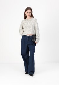 Maglione grigio chiaro a maniche corte con un motivo a maglia testurizzato, abbinato a jeans a gamba larga blu scuro e scarpe nere senza lacci.