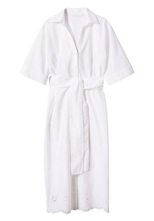 Vrouw draagt een witte midi-jurk met knopen aan de voorkant, ellebooglange mouwen, een tailleband, een zoom met opengewerkt motief en bruine sandalen met open tenen en hak.