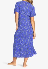 Robe maxi bleue avec un motif floral blanc, à manches courtes et à coupe décontractée, fabriquée en tissu doux, avec un ourlet atteignant sous les chevilles.