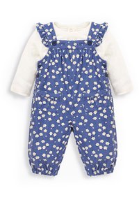 Blaue floral bedruckte Latzhose mit Rüschenträgern, Muster aus gelben Gänseblümchen, zwei Vorderaschen, elastische Ärmelbündchen, schichtweise über einem weißen Langarmshirt.